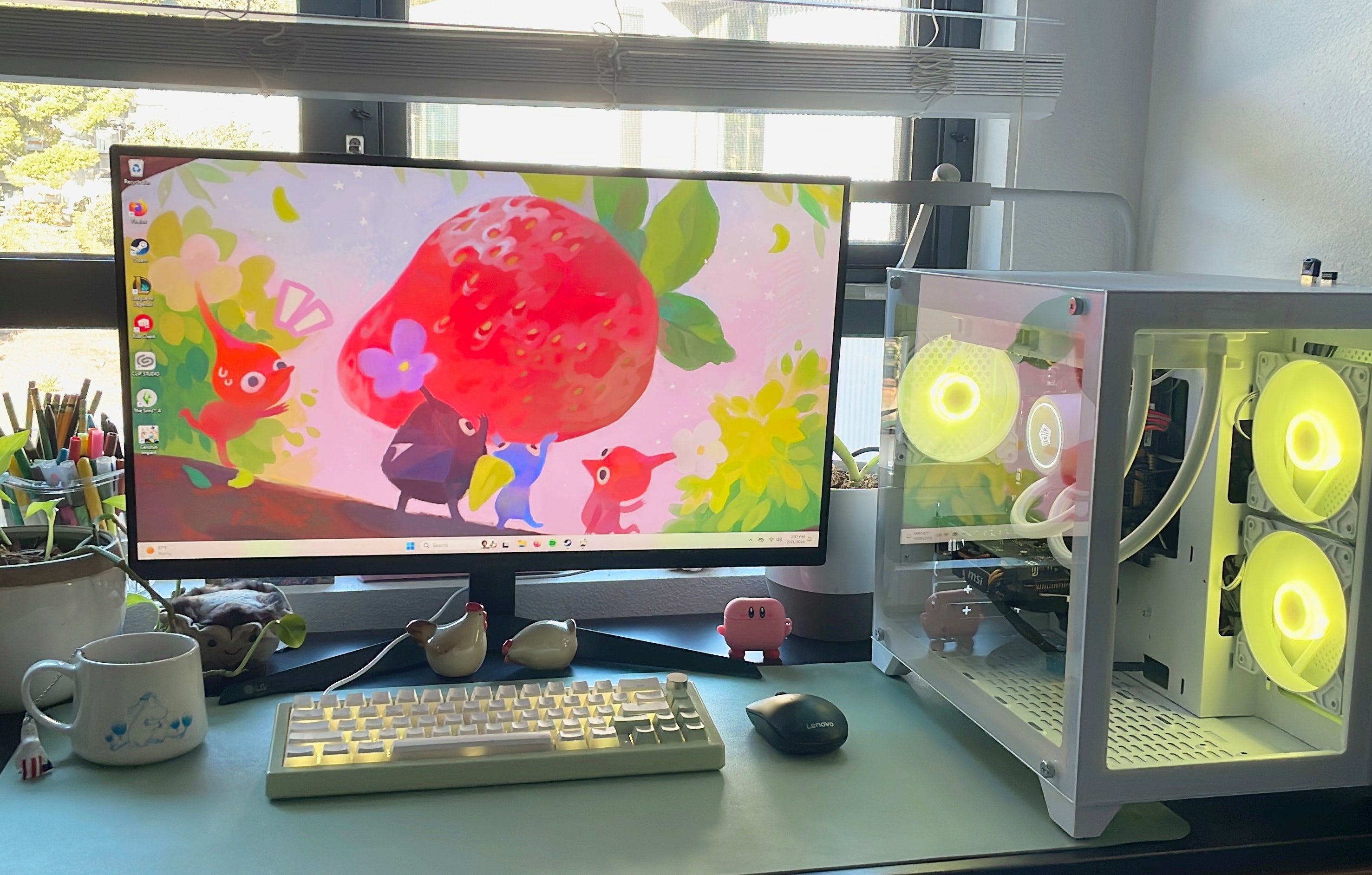 A PC setup. It includes a monitor with a background of Pikmin carrying a strawberry, a green keyboard, a black mouse, and the PC itself, which has two clear glass sides and fans with yellow light.